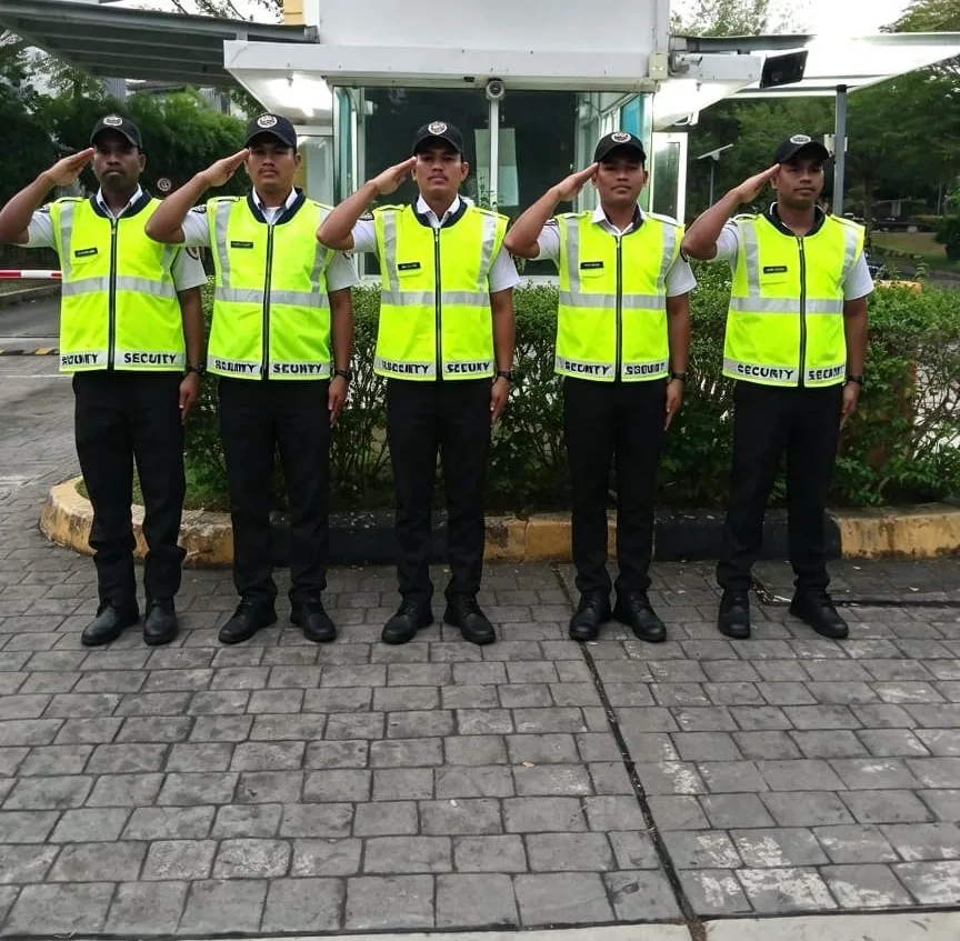 Five guards in hi-visibility vests saluting outside a township guardhouse